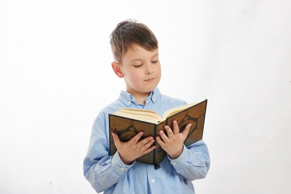 Online Quran classes for kids – A young boy reading the Holy Quran with focus. Learn Quran online with professional tutors from Al Quran Online Academy.